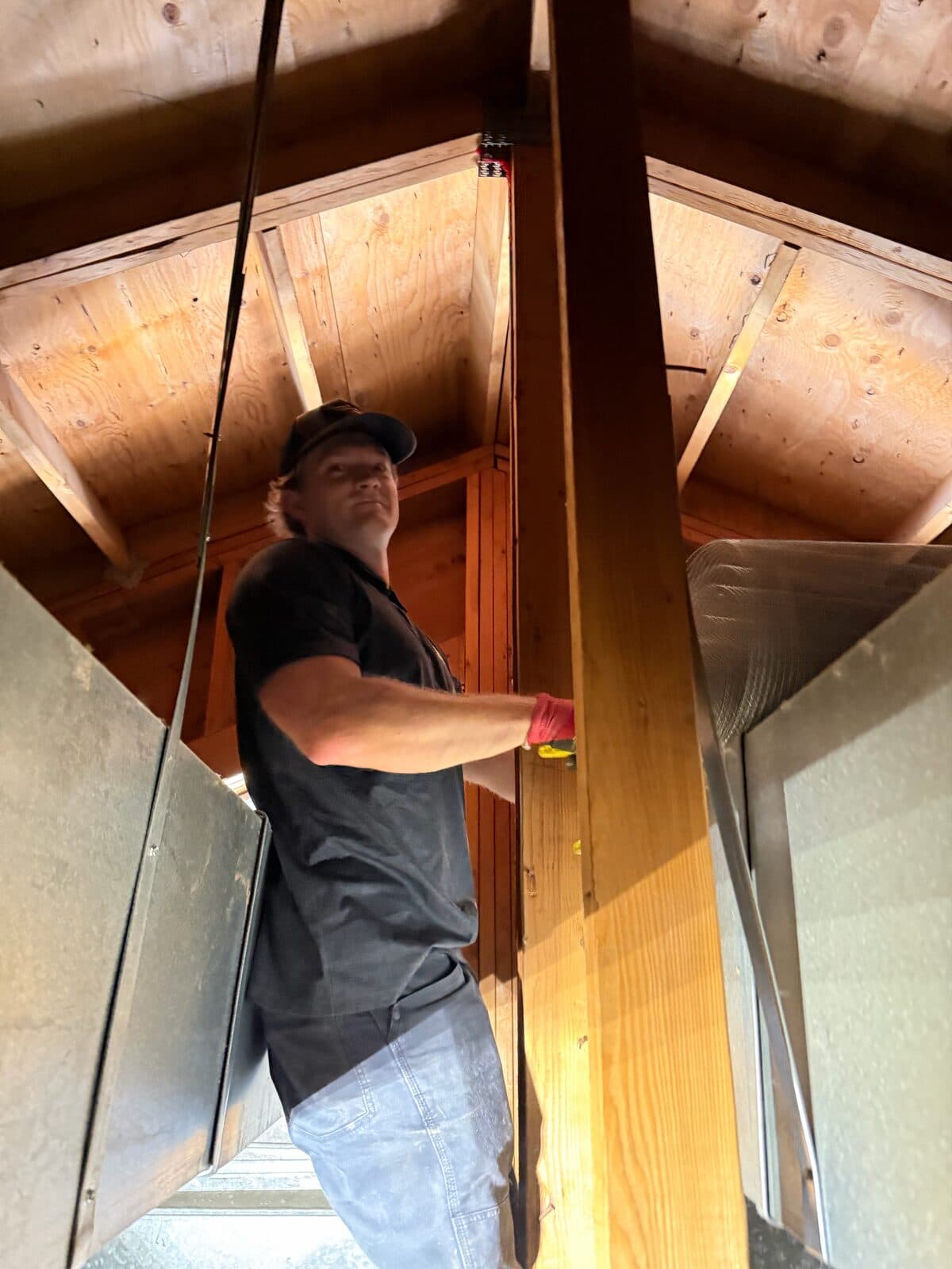 Technician in a wood attic beside framing and ductwork during inspection